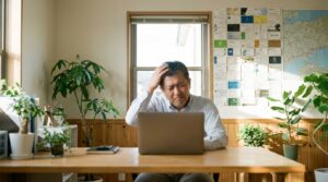 岡山県の中小企業オフィスで、50代の男性経営者がノートパソコンの前で少し困った表情をしている。壁には地元の取引先の名刺。朝の柔らかい光、写真風、顔はぼかす、清潔感のある空間