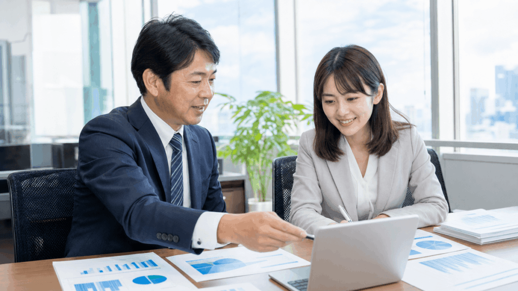 日本人の40代男性経営者と20代の若手女性スタッフが、明るいオフィスでノートパソコンとグラフ資料を一緒に見ながら前向きに打ち合わせをしている場面。デスクには数字の資料。写真風、明るく華やかな雰囲気、ドキュメンタリーテイスト